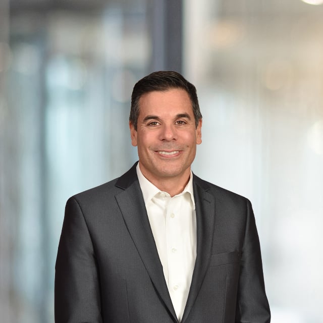 Portrait of a man in a suit smiling, blurred background.