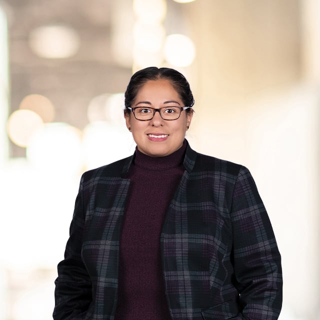 Professional woman wearing glasses, blazer, and maroon turtleneck.