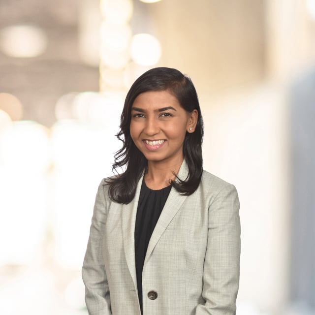 Woman in a blazer smiling in front of a blurred background.