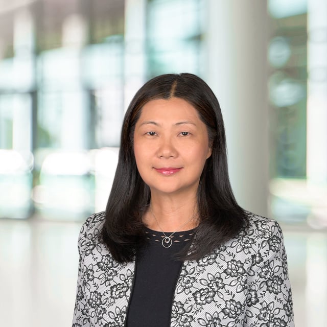 Asian woman with dark hair and a patterned jacket smiling.
