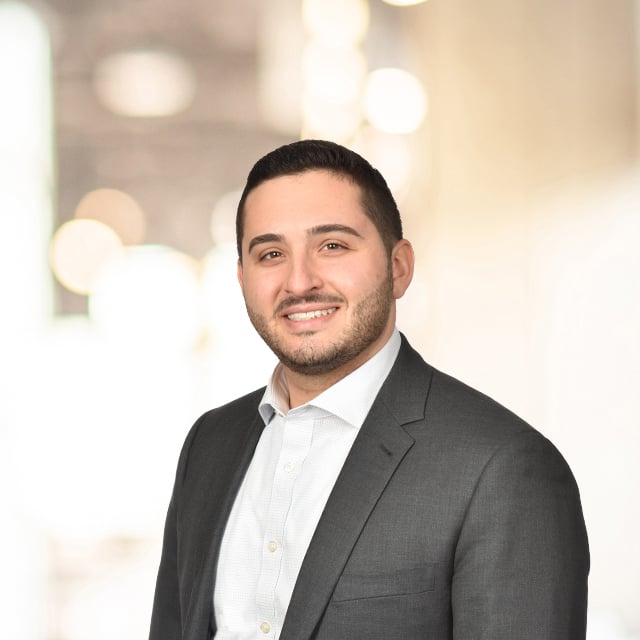 Smiling man in a suit stands in front of a blurred background.