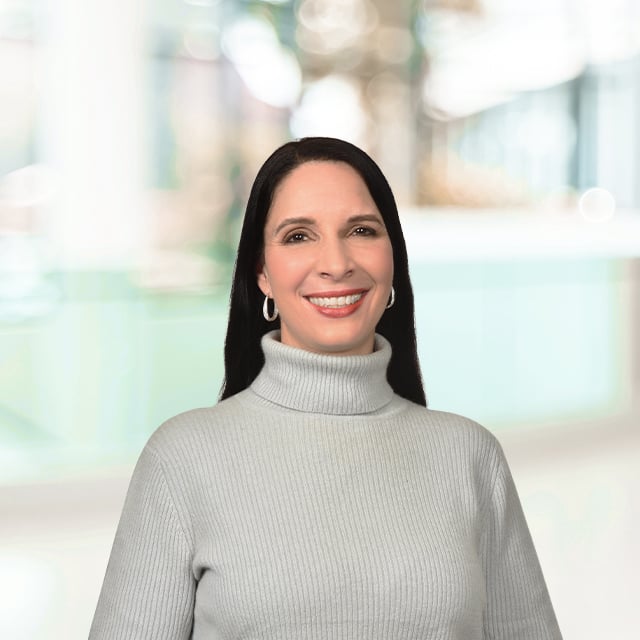 Woman in a light gray turtleneck with a blurred background.