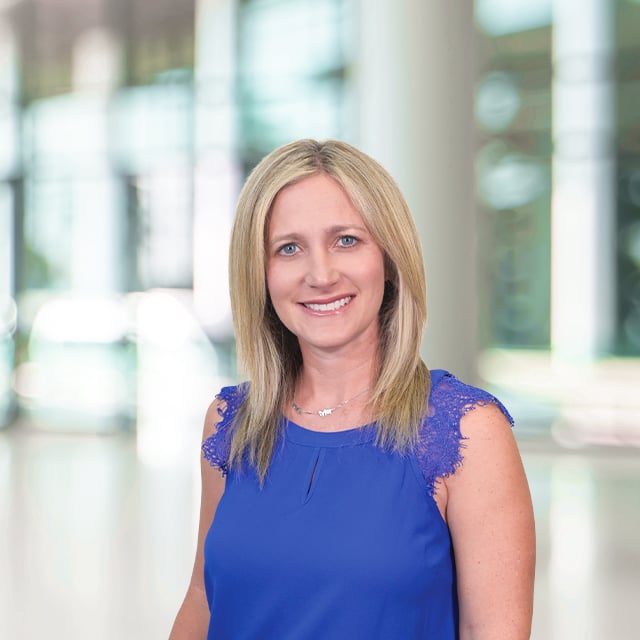 Woman in blue top smiles in an office setting.