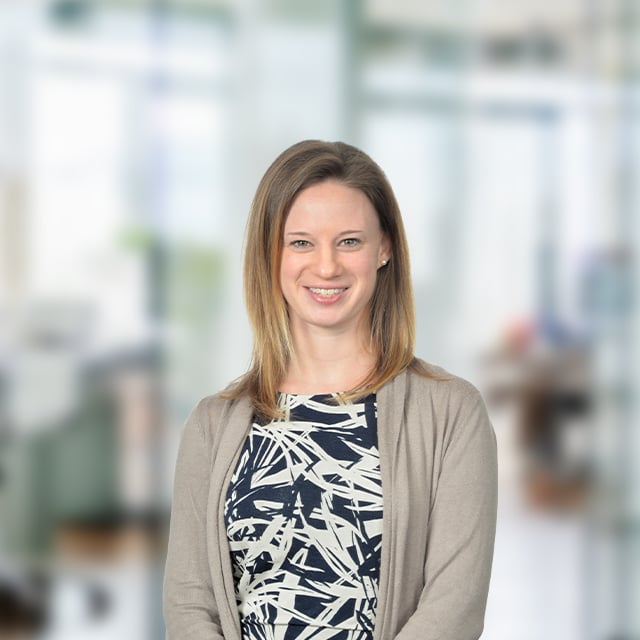 A woman smiling in an office setting, wearing a blouse and cardigan.