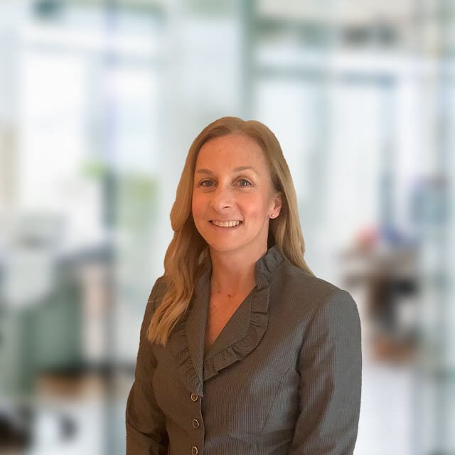 Woman in blazer smiling in an office setting.