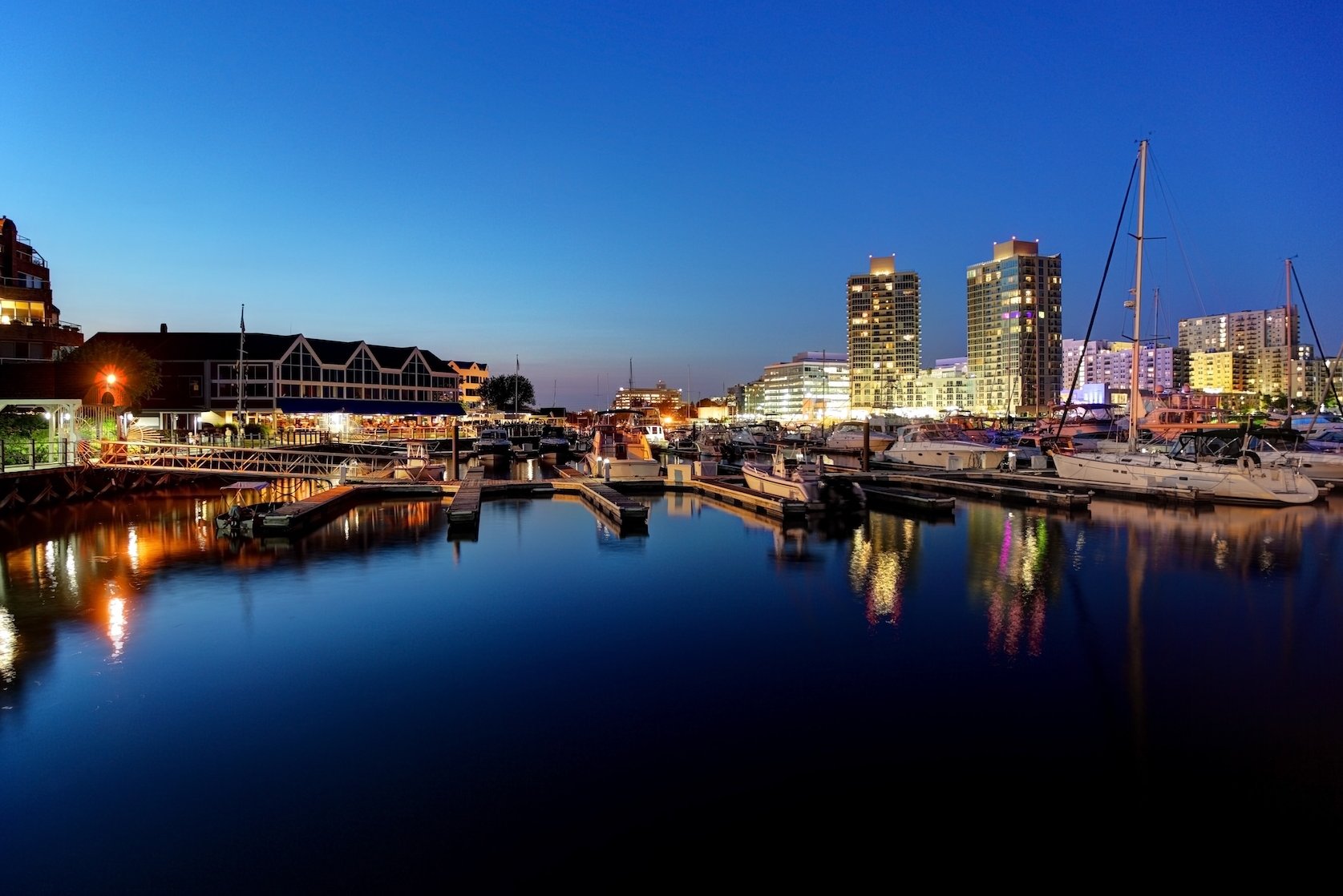 Harbor at dusk with boats, buildings, and lights reflecting in the water.