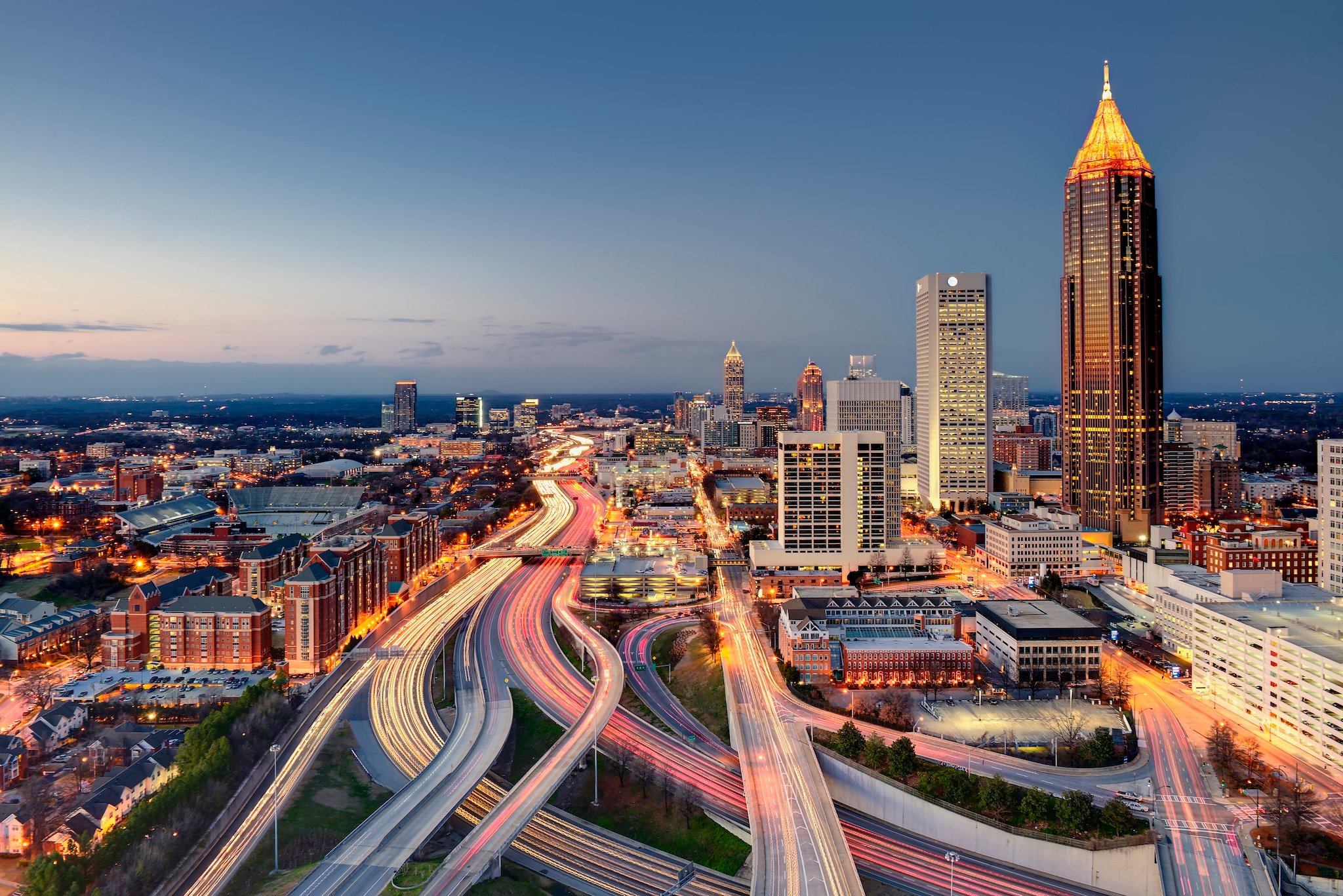 Cityscape with skyscrapers, illuminated highways, and lights at dusk.