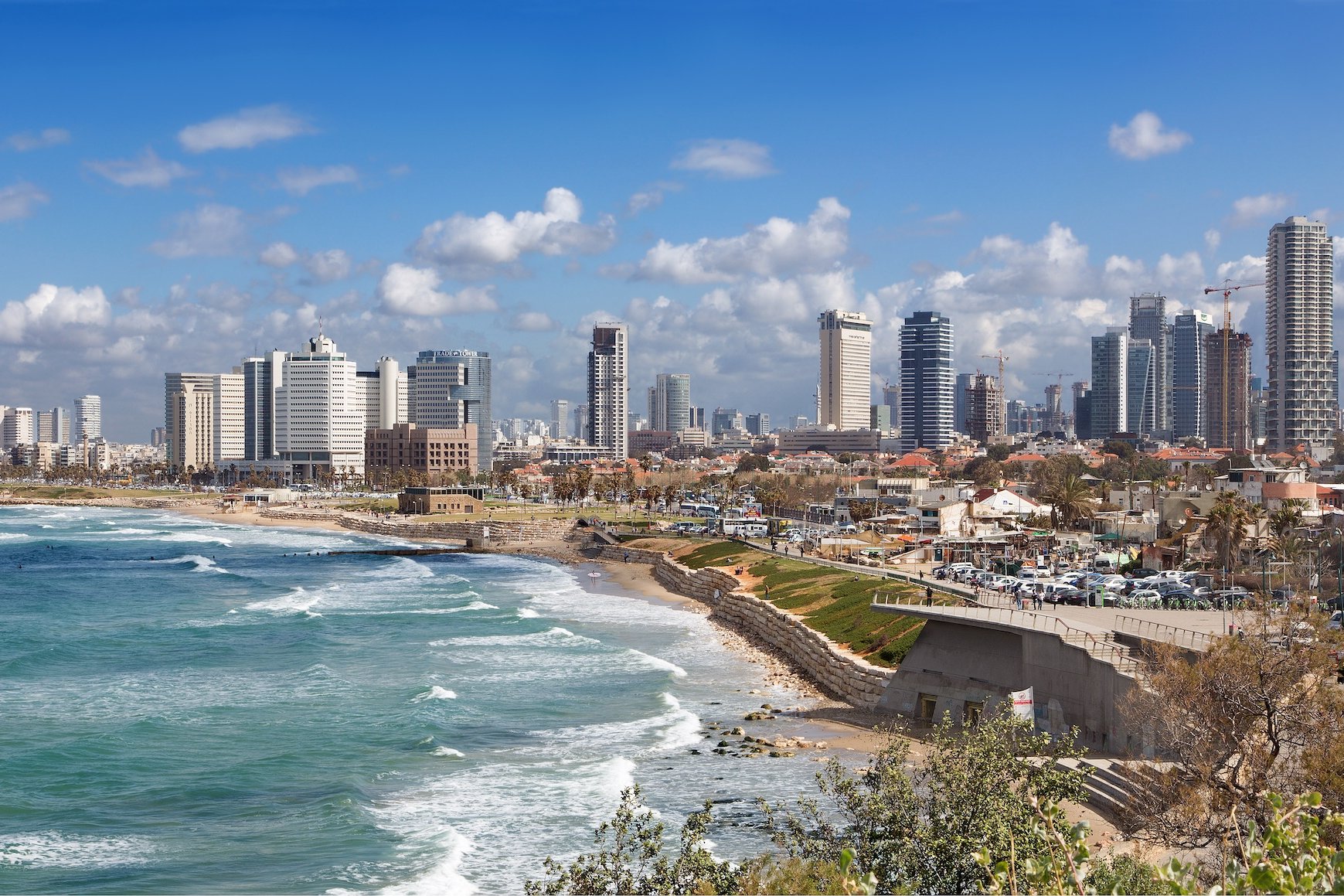 Coastal city with high-rise buildings and beach, blue sky with clouds.
