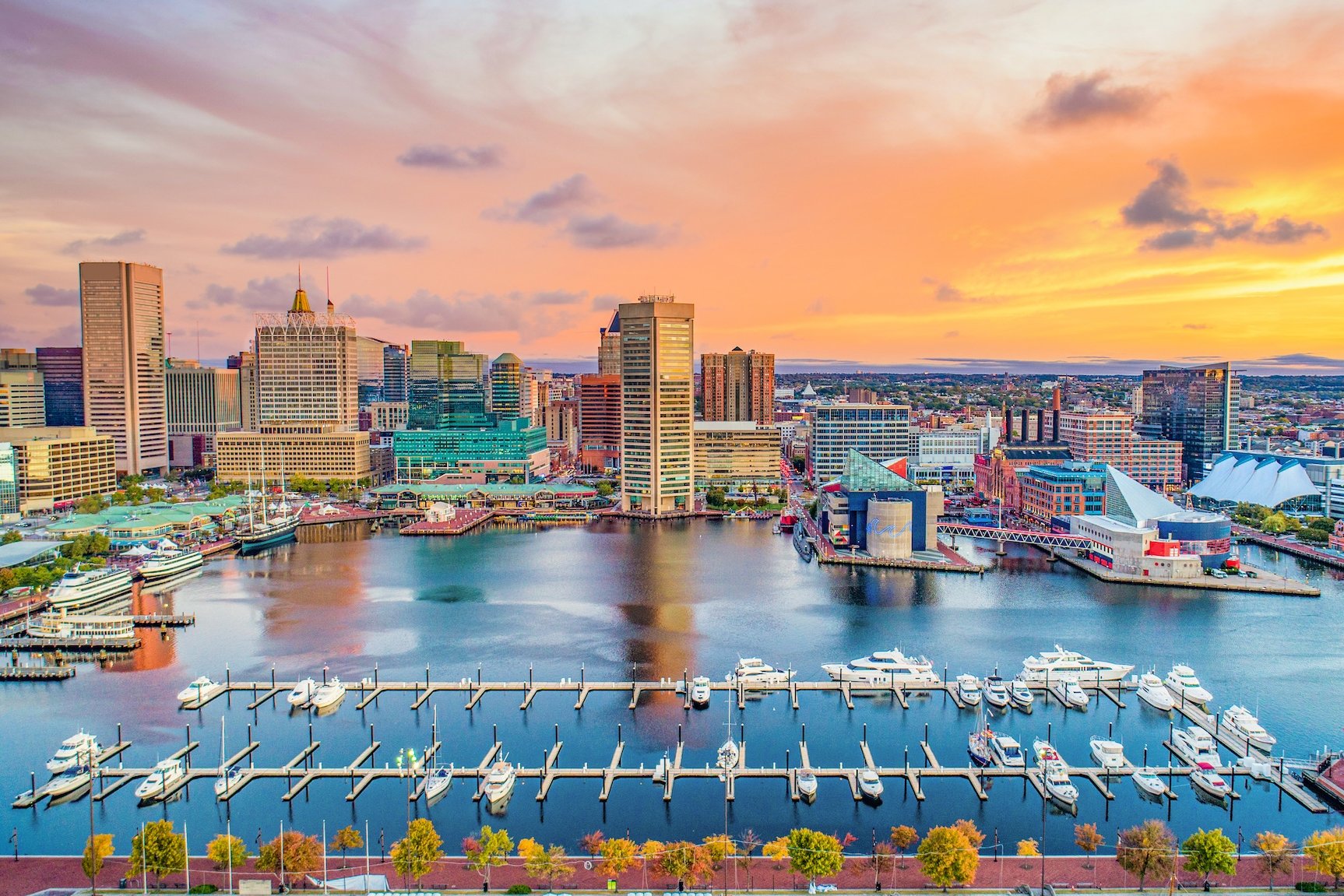 Aerial view of Baltimore's harbor with boats, buildings, and an orange sky.