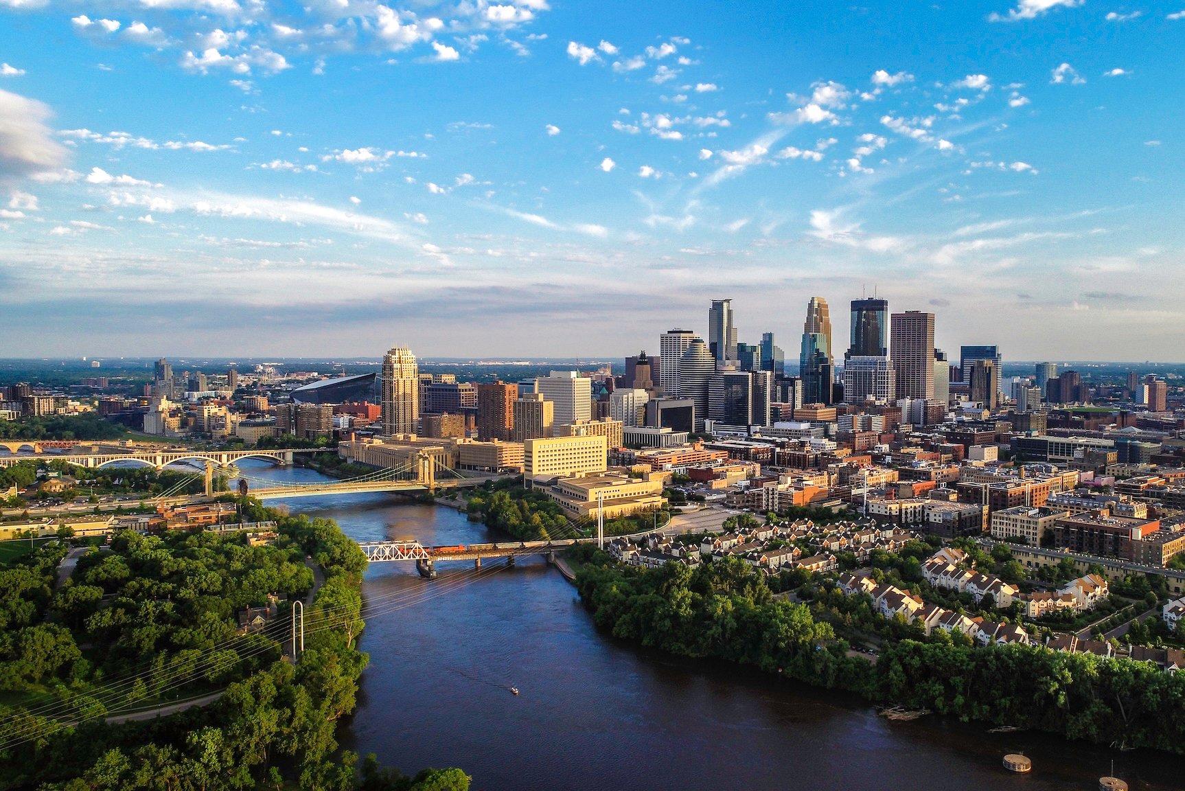 Aerial view of Minneapolis with a river, bridges, and city buildings under a blue sky.
