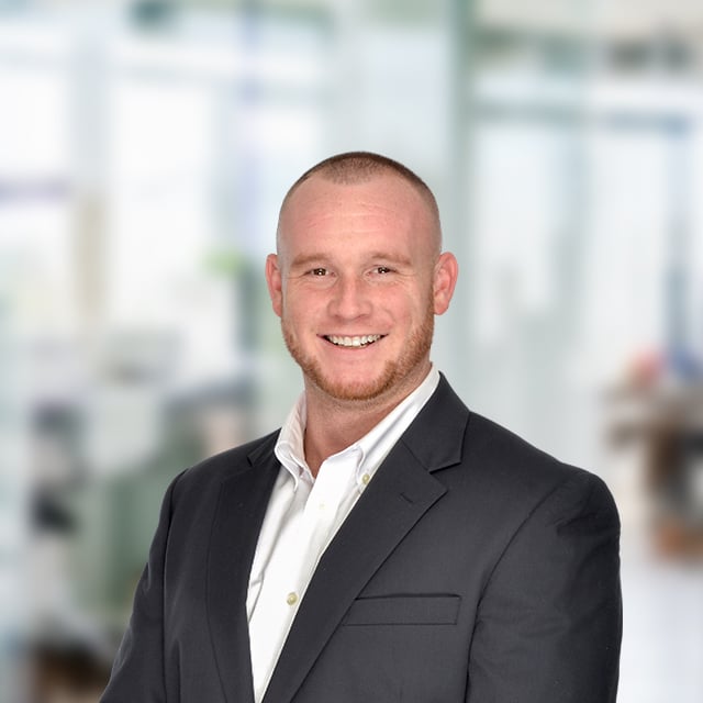 Portrait of a smiling man in a suit, with a blurred office background.