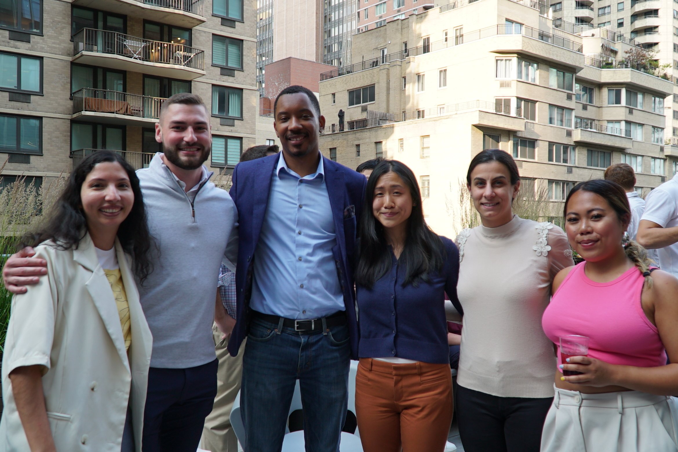 Diverse group smiling at an outdoor gathering, urban backdrop.