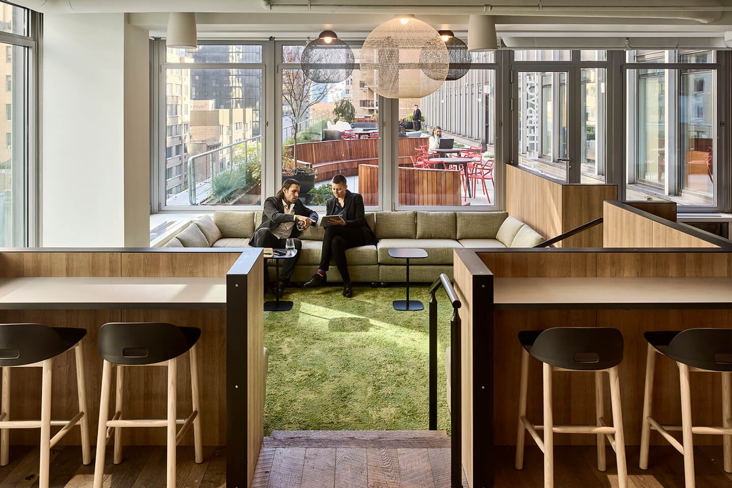 Two businesspeople in an office lounge area with a view of a terrace.