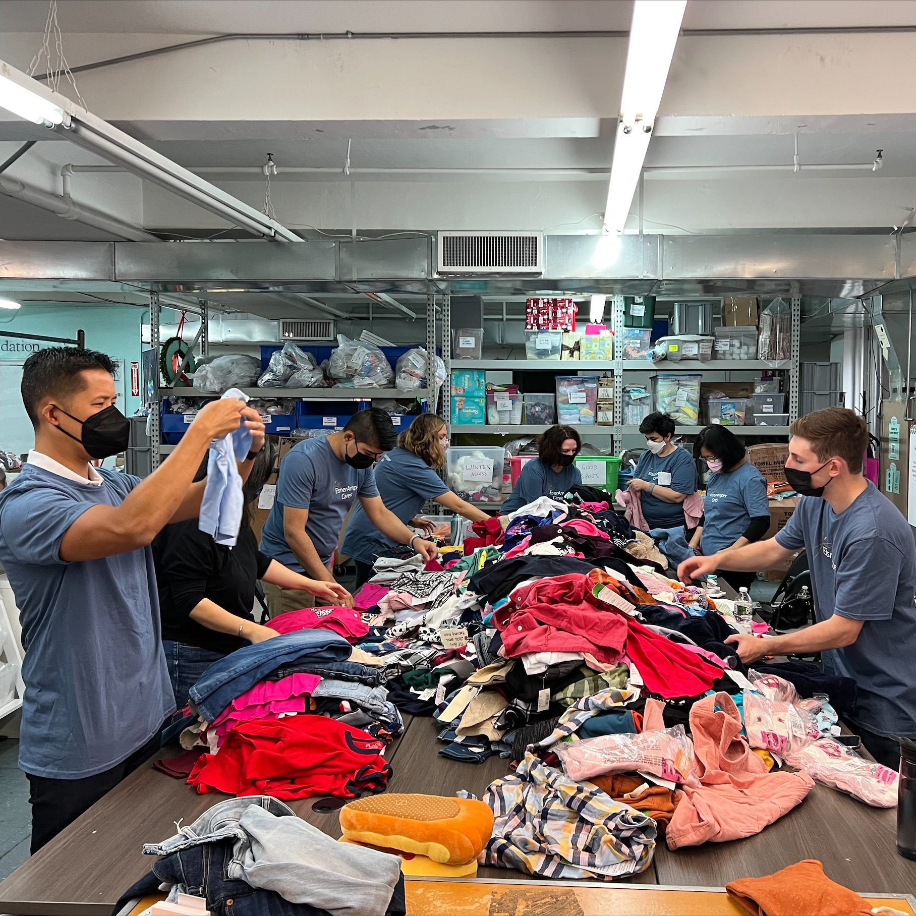 People wearing masks sorting through piles of clothes at a community event.