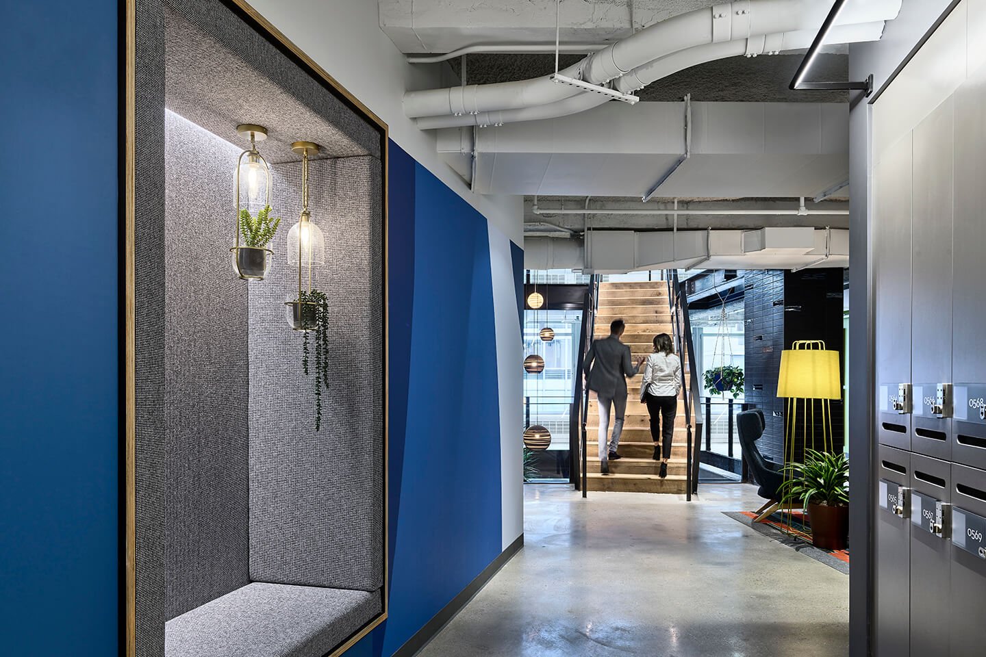 Two people walking up stairs. Blue wall with plants. Modern design.