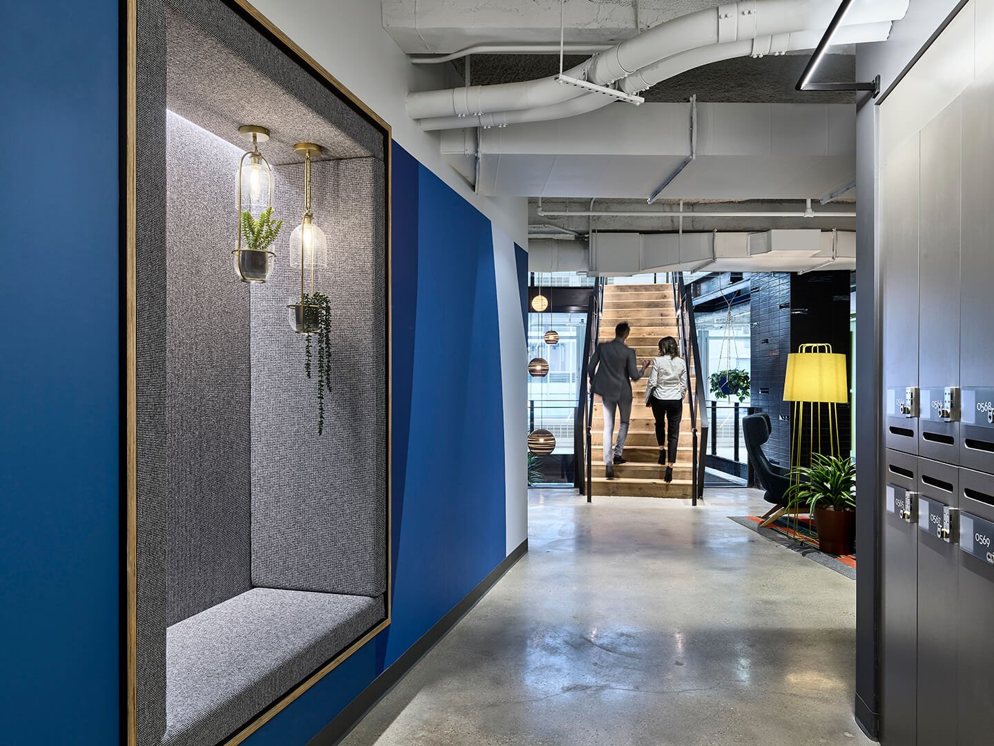 Two people walking up stairs. Blue wall with plants. Modern design.