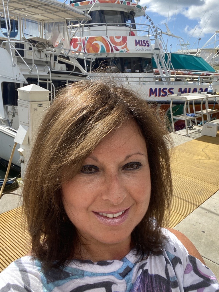 Woman in front of a boat, smiling at the camera. Boat says "Miss Sarah Bean, Miss Miami".