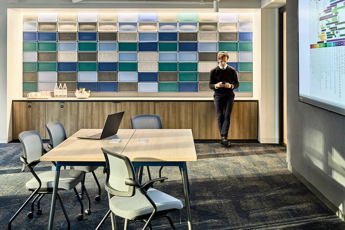 Man standing in a modern office. Meeting table with laptop and chairs, colorful wall.