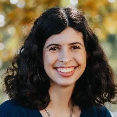 Portrait of a smiling woman with dark hair, blurred background.