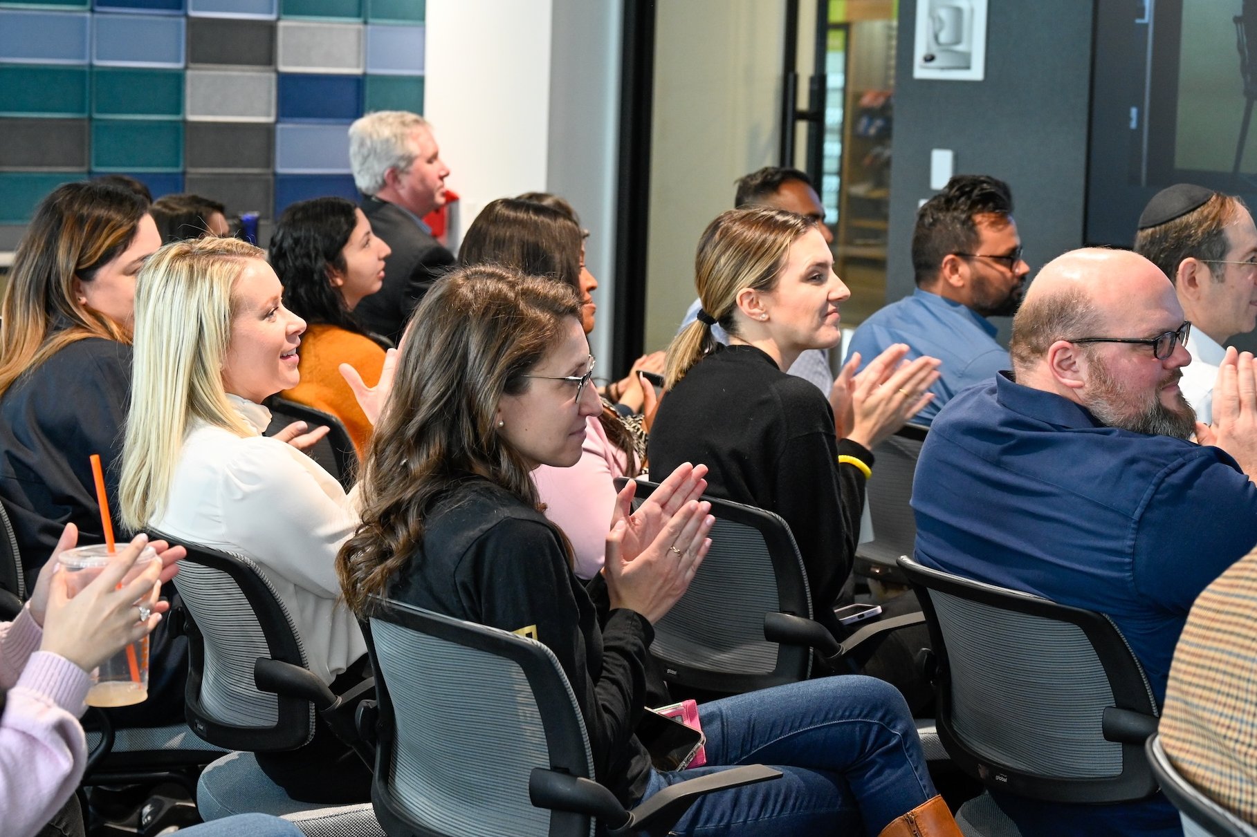 People clapping during a presentation; some with drinks.