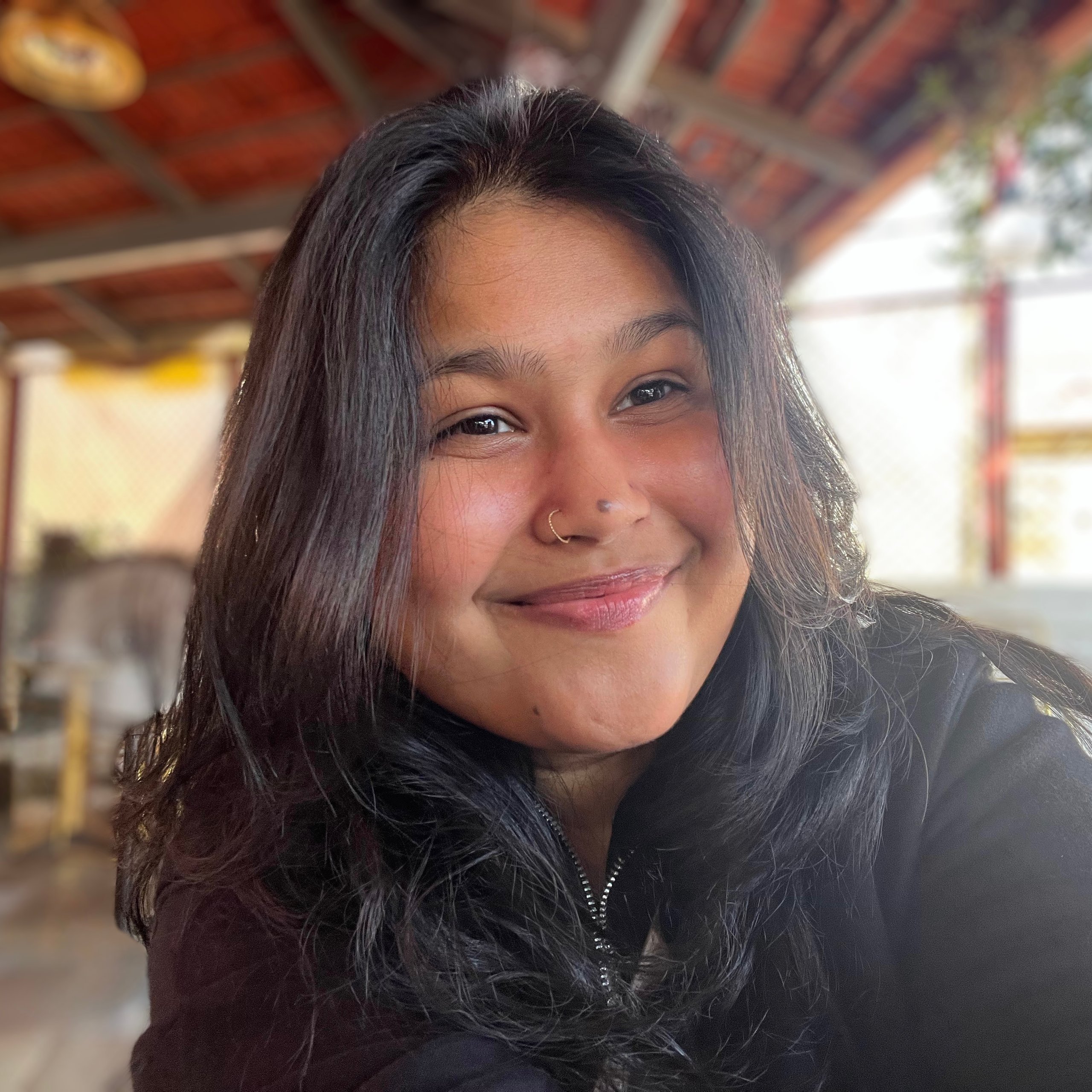 Woman with nose ring smiling; outdoors, blurry background.